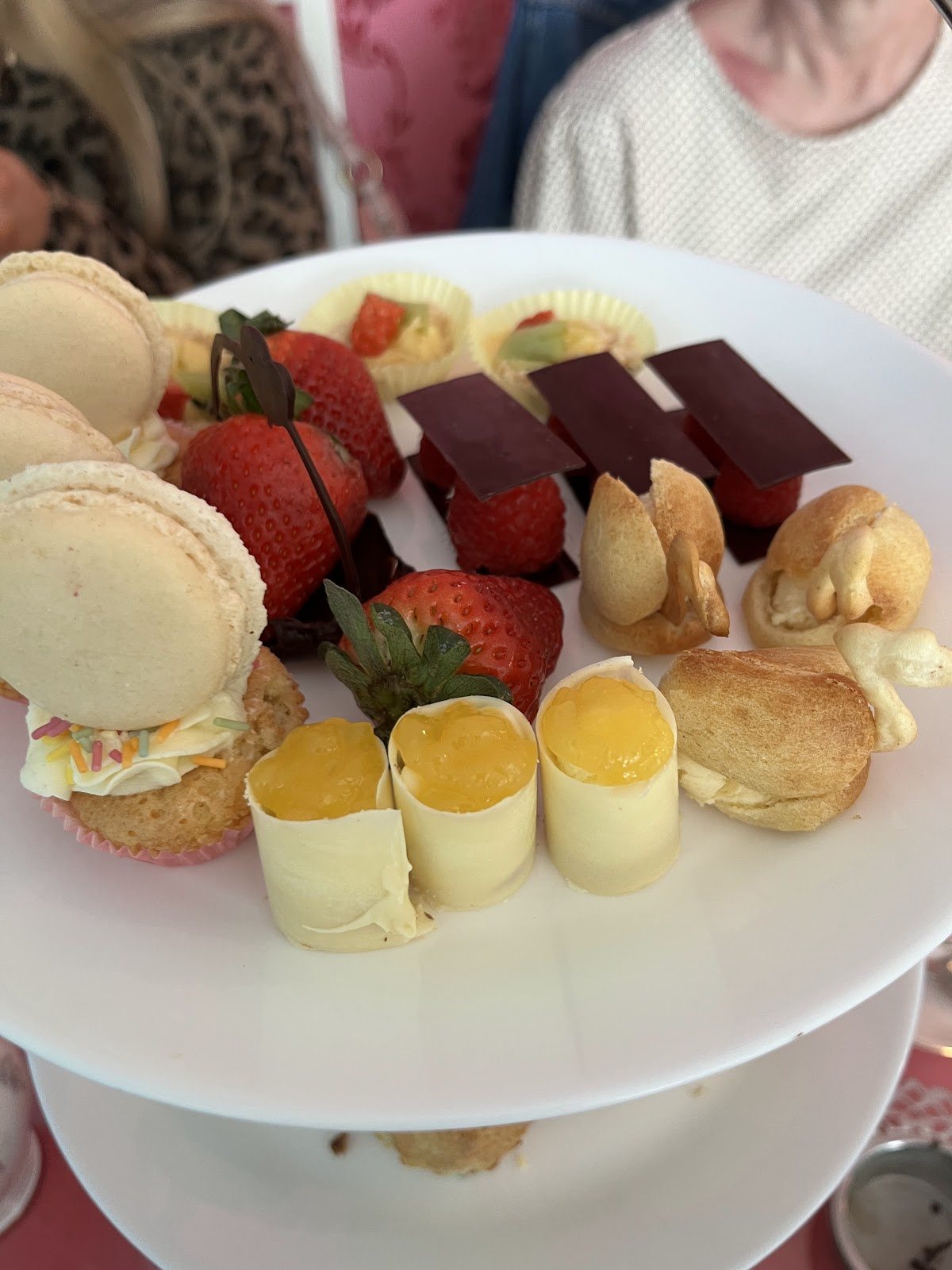 Close-up of the top tier: macarons, lemon-curd rolls, strawberries, chocolate squares and choux pastry swans.